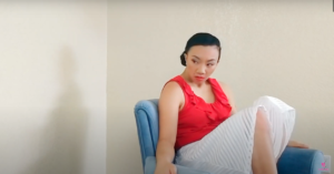Filipino woman with a low bun. Red top with white skirt. Woman sitting on a light blue chair.